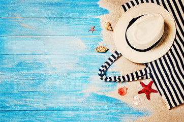 Top view of sandy beach with blue marine planks frame and summer accessories. Background with copy space and visible sand and wood texture. Border composition