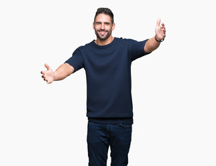 Young handsome man wearing sweater over isolated background looking at the camera smiling with open arms for hug. Cheerful expression embracing happiness.