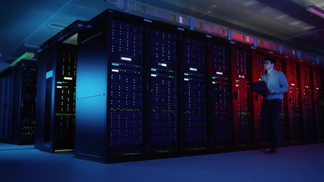 In Data Center: Male IT Specialist Walks along the Row of Operational Server Racks, Uses Laptop for Maintenance. Concept for Telecommunications, Cloud Computing, Artificial Intelligence, Supercomputer