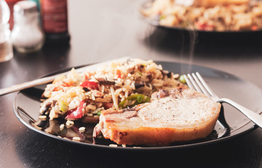 A vintage style close-up of a pork chop served with fried brown rice and vegetables