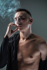 Young man inhaling a rich cloud of smoke, studio image