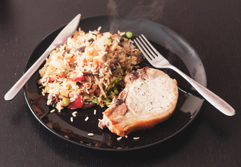 A vintage style overhead image of a pork chop served with fried brown rice and vegetables