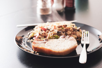 A vintage style image of a pork chop served with fried brown rice and vegetables
