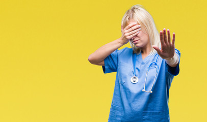 Young beautiful blonde doctor woman wearing medical uniform over isolated background covering eyes...