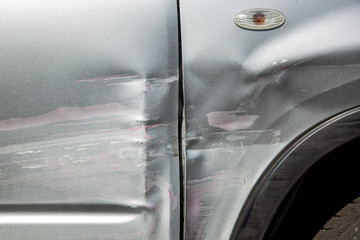 scratched car door and fender after an accident, close up car body damage scratches and blow in the side of the gray car.