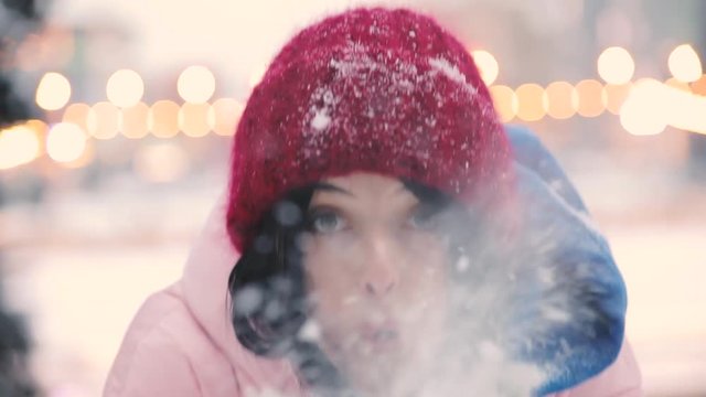 Happy woman blowing snow from hands at winter, slowmotion