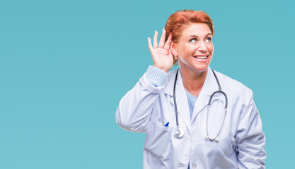 Senior caucasian doctor woman wearing medical uniform over isolated background smiling with hand over ear listening an hearing to rumor or gossip. Deafness concept.