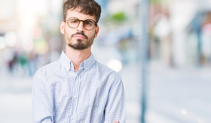 Young handsome man wearing glasses over isolated background skeptic and nervous, disapproving expression on face with crossed arms. Negative person.
