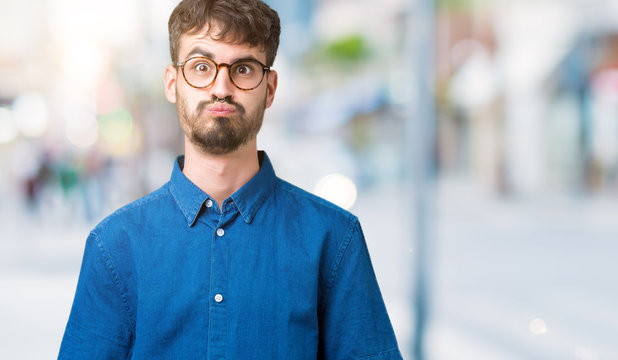 Young handsome man wearing glasses over isolated background puffing cheeks with funny face. Mouth inflated with air, crazy expression.
