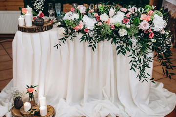 Wedding banquet. The festive table for the newlyweds is decorated with a beautiful composition of various flowers,  greenery and candle