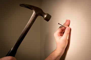 Man's hands prepare to hit a nail with a hammer; on blank wall for picture hanging.