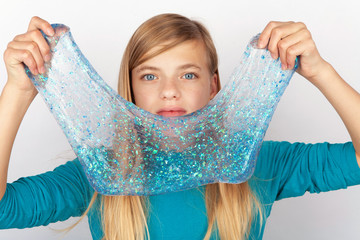Beautiful young girl holding a glitter slime in front of her face