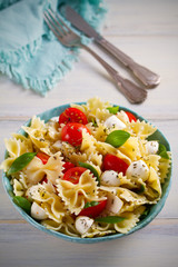 Caprese Pasta Salad. Pasta with mozzarella cheese, tomatoes and basil in bowl on wooden table. vertical