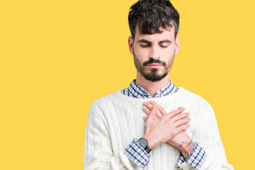 Young handsome man wearing winter sweater over isolated background smiling with hands on chest with closed eyes and grateful gesture on face. Health concept.