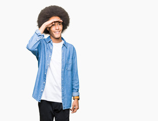 Young african american man with afro hair very happy and smiling looking far away with hand over head. Searching concept.