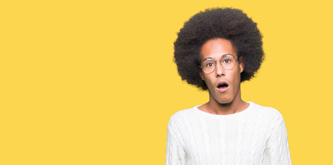Fototapeta na wymiar Young african american man with afro hair wearing glasses In shock face, looking skeptical and sarcastic, surprised with open mouth