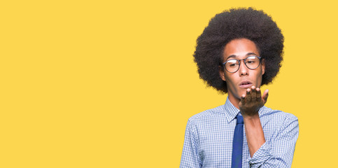Young african american business man with afro hair wearing glasses looking at the camera blowing a kiss with hand on air being lovely and sexy. Love expression.