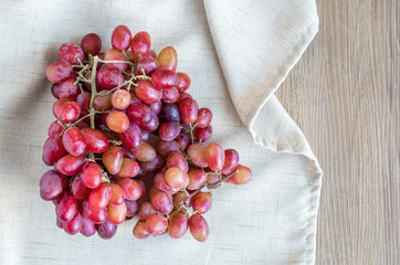 a bunch of red and purple grapes in a tan linen cloth on a wooden table with copy space