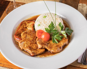 Böhmische Küche, Schweinsbraten mit Reis - Angerichtet auf einem Holztisch in weißem Teller