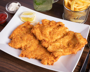 Böhmische Küche, Wiener Schnitzel - Angerichtet auf einem Holztisch in weißem Teller mit Pommes
