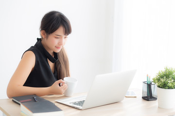 Fototapeta premium Beautiful young freelance asian woman smiling working and on laptop computer at desk office with professional, girl using notebook and drink coffee, business and lifestyle concept.