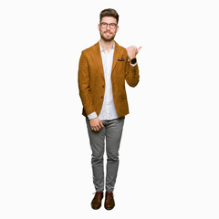 Young handsome business man wearing glasses smiling with happy face looking and pointing to the side with thumb up.