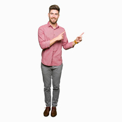 Young handsome business casual man smiling and looking at the camera pointing with two hands and fingers to the side.