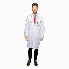 Young handsome doctor man wearing medical coat winking looking at the camera with sexy expression, cheerful and happy face.