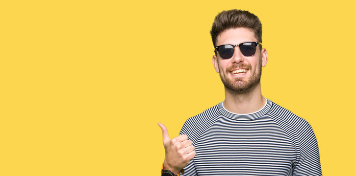 Young handsome man wearing sunglasses doing happy thumbs up gesture with hand. Approving expression looking at the camera with showing success. - Powered by Adobe