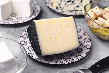 piece of Spanish sheep cheese and other types of cheese on gray marbled background
