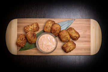 Fried nuggets with sauce, on a wooden board with a bamboo leaf, top view