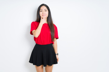 Beautiful brunette woman wearing red t-shirt and skirt over isolated background looking confident at the camera with smile with crossed arms and hand raised on chin. Thinking positive.