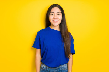 Beautiful brunette woman wearing blue t-shirt over yellow isolated background with a happy and cool smile on face. Lucky person.