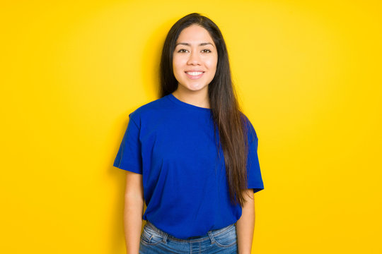 Beautiful brunette woman wearing blue t-shirt over yellow isolated background with a happy and cool smile on face. Lucky person.