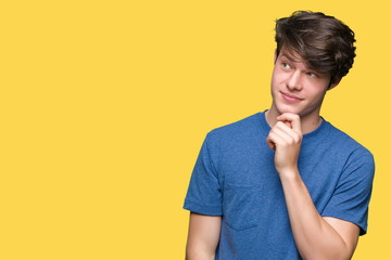 Young handsome man wearing blue t-shirt over isolated background with hand on chin thinking about...