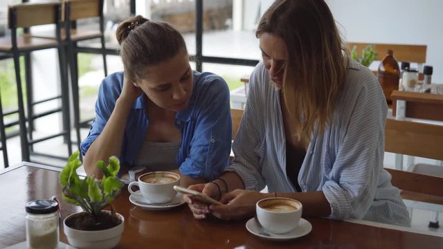 Women having date in cafe. One Sharing something Exciting on her Mobile Phone