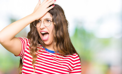 Young beautiful woman wearing glasses surprised with hand on head for mistake, remember error....