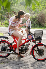 Portrait of happy mother with her baby girl sitting on the red bicycle in the park during a nice summer day
