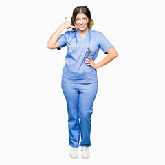 Young adult doctor woman wearing medical uniform smiling doing phone gesture with hand and fingers like talking on the telephone. Communicating concepts.