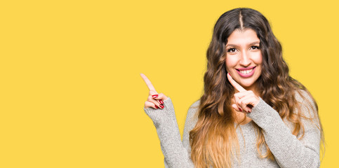 Naklejka premium Young beautiful woman wearing winter dress smiling and looking at the camera pointing with two hands and fingers to the side.