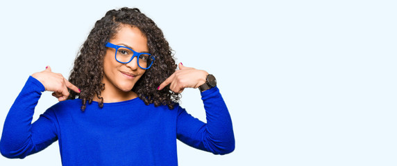Young beautiful woman with curly hair wearing glasses looking confident with smile on face,...
