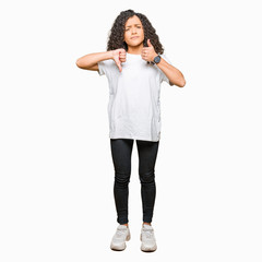 Young beautiful woman with curly hair wearing white t-shirt Doing thumbs up and down, disagreement and agreement expression. Crazy conflict