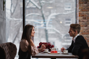 Young couple in love, man and woman, sit at a table in a cafe. St. Valentine's Day.