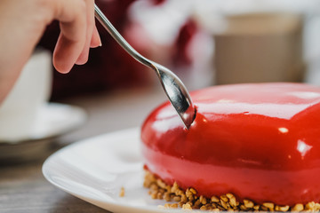 Red cake in the shape of a heart is on the table. Two hands with spoons, male and female, stretch into a pie.
