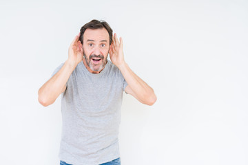 Fototapeta premium Handsome senior man over isolated background Trying to hear both hands on ear gesture, curious for gossip. Hearing problem, deaf