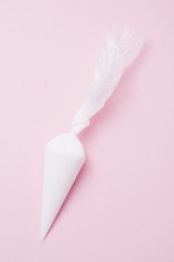 Close up of colored piping bag with pink  frosting inside opened and used over a pink background