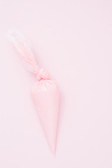 Close up of colored piping bag with pink  frosting inside opened and used over a pink background