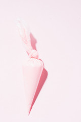 Close up of colored piping bag with pink  frosting inside opened and used over a pink background