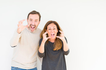 Beautiful middle age couple in love over isolated background Shouting frustrated with rage, hands trying to strangle, yelling mad