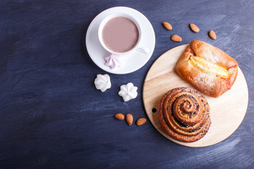 a cup of hot chocolate and buns  on black wooden background.